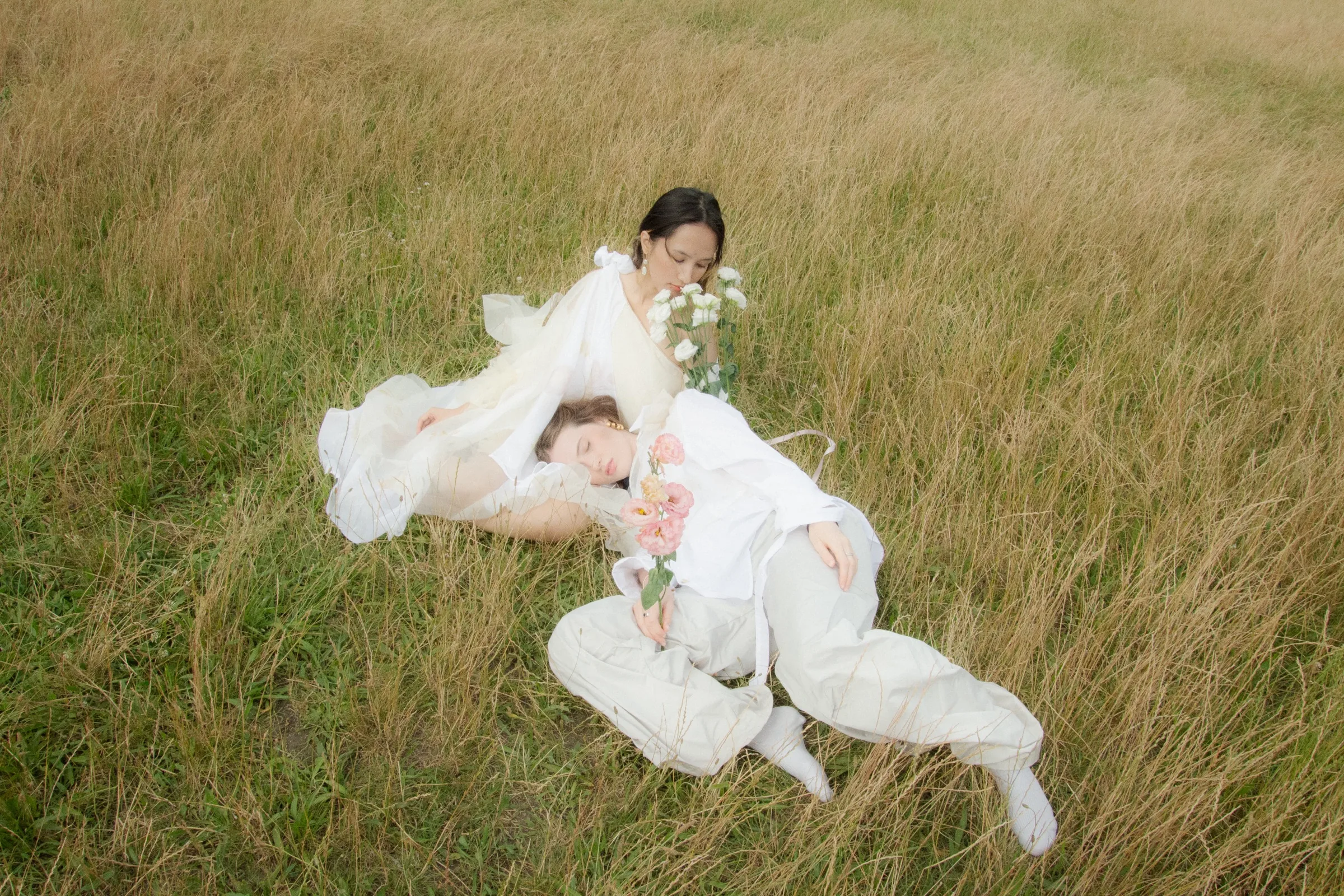 Two figures in white rest in a sunlit meadow, seen from above