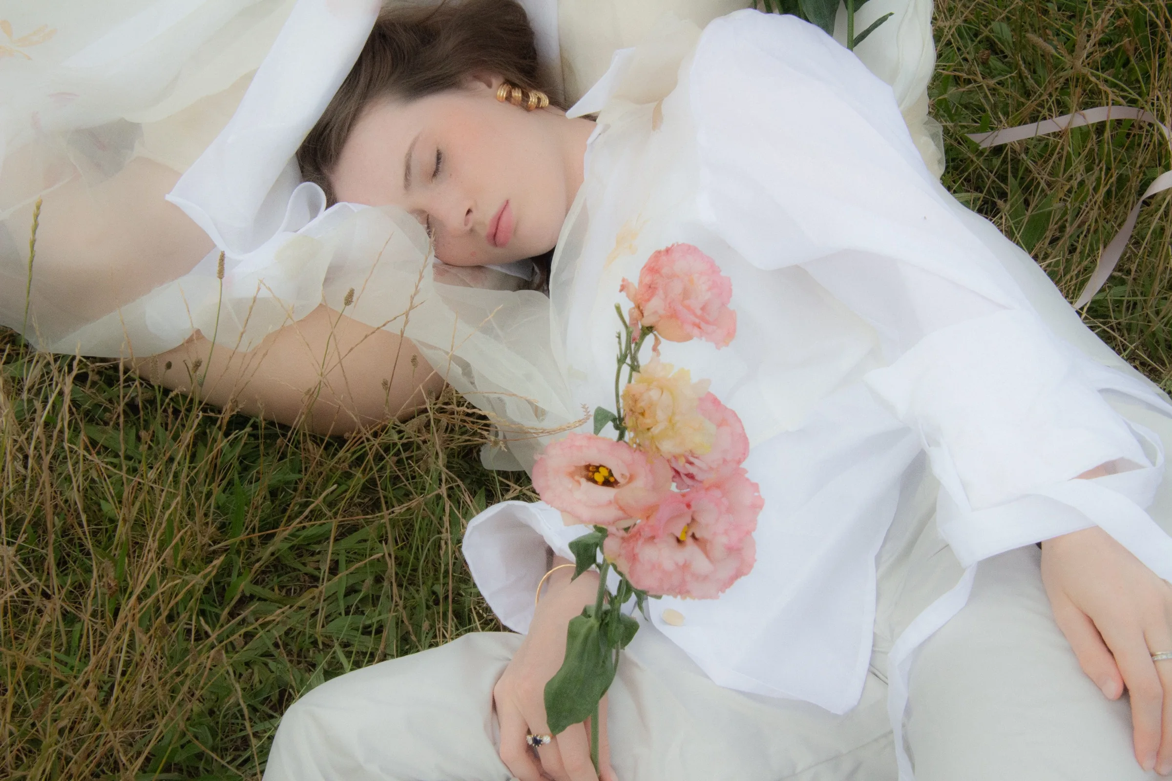 A model sleeps among the grass, pink ranunculus resting on a white shirt