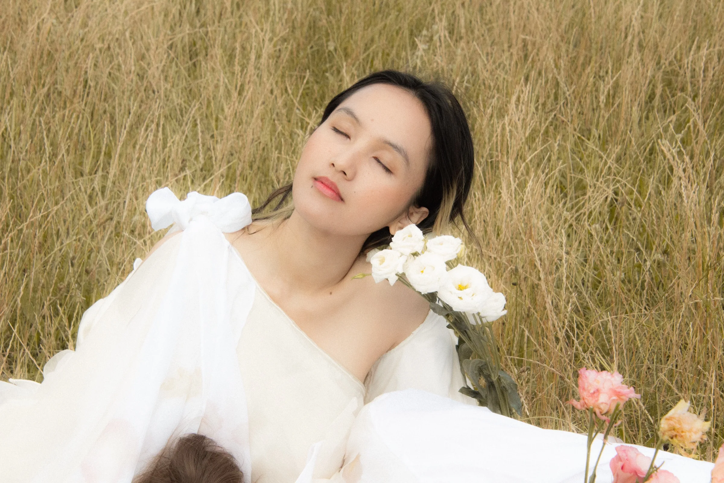 A model reclines with eyes closed, an off-shoulder organza gown loosened to the light