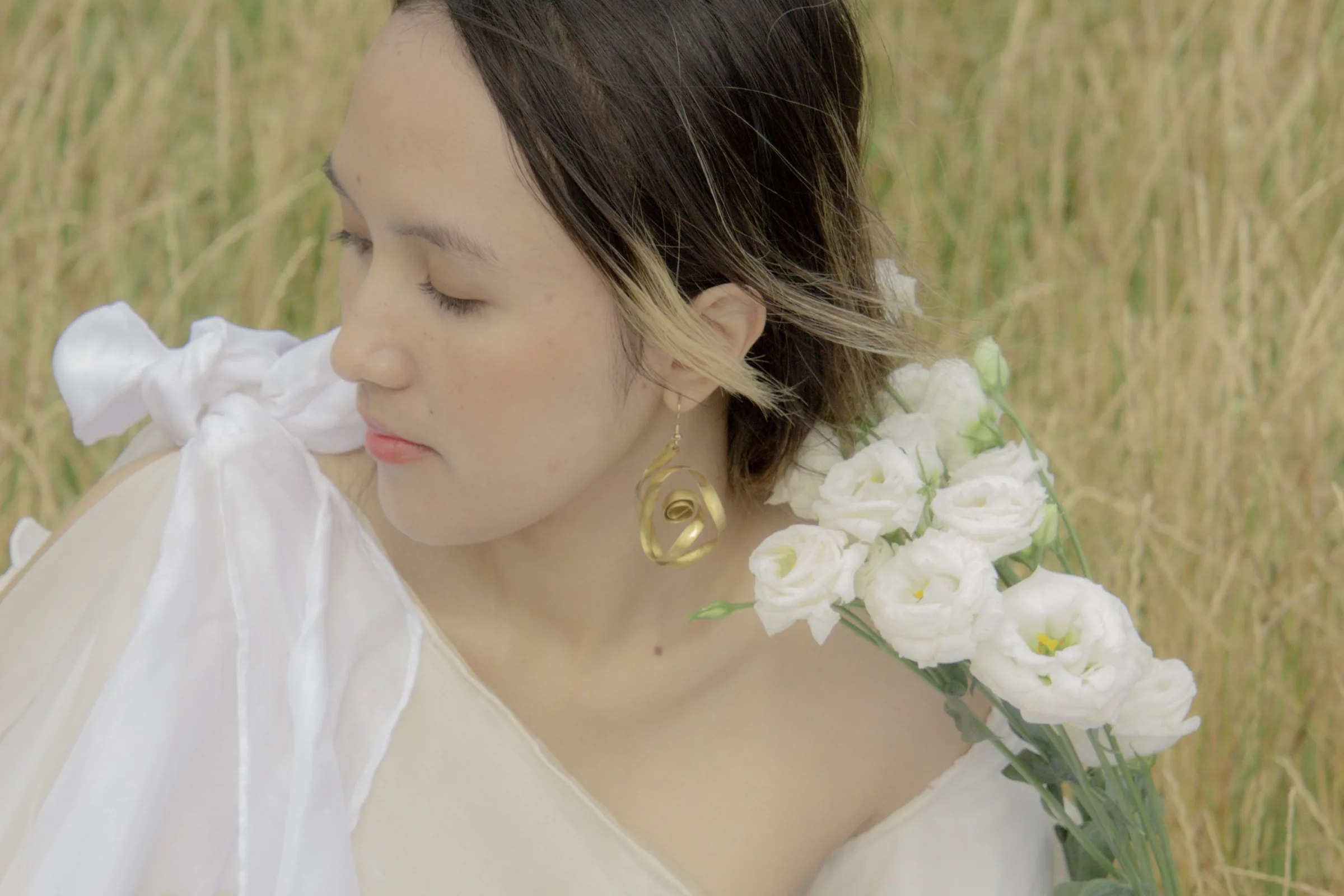 Profile close-up, a gold rose earring beside a spray of white lisianthus