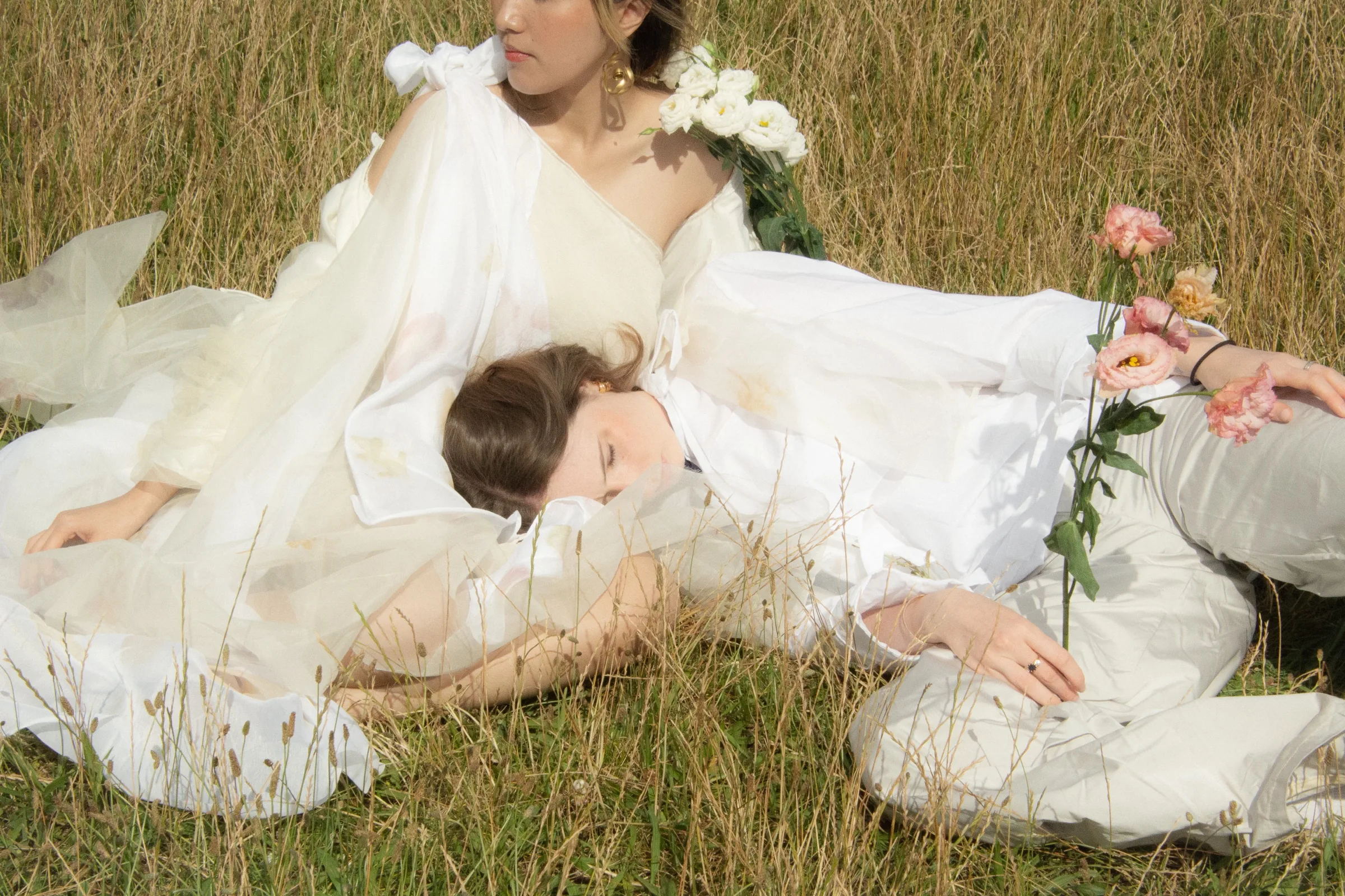 Two models entwined in the grass beneath layers of tulle