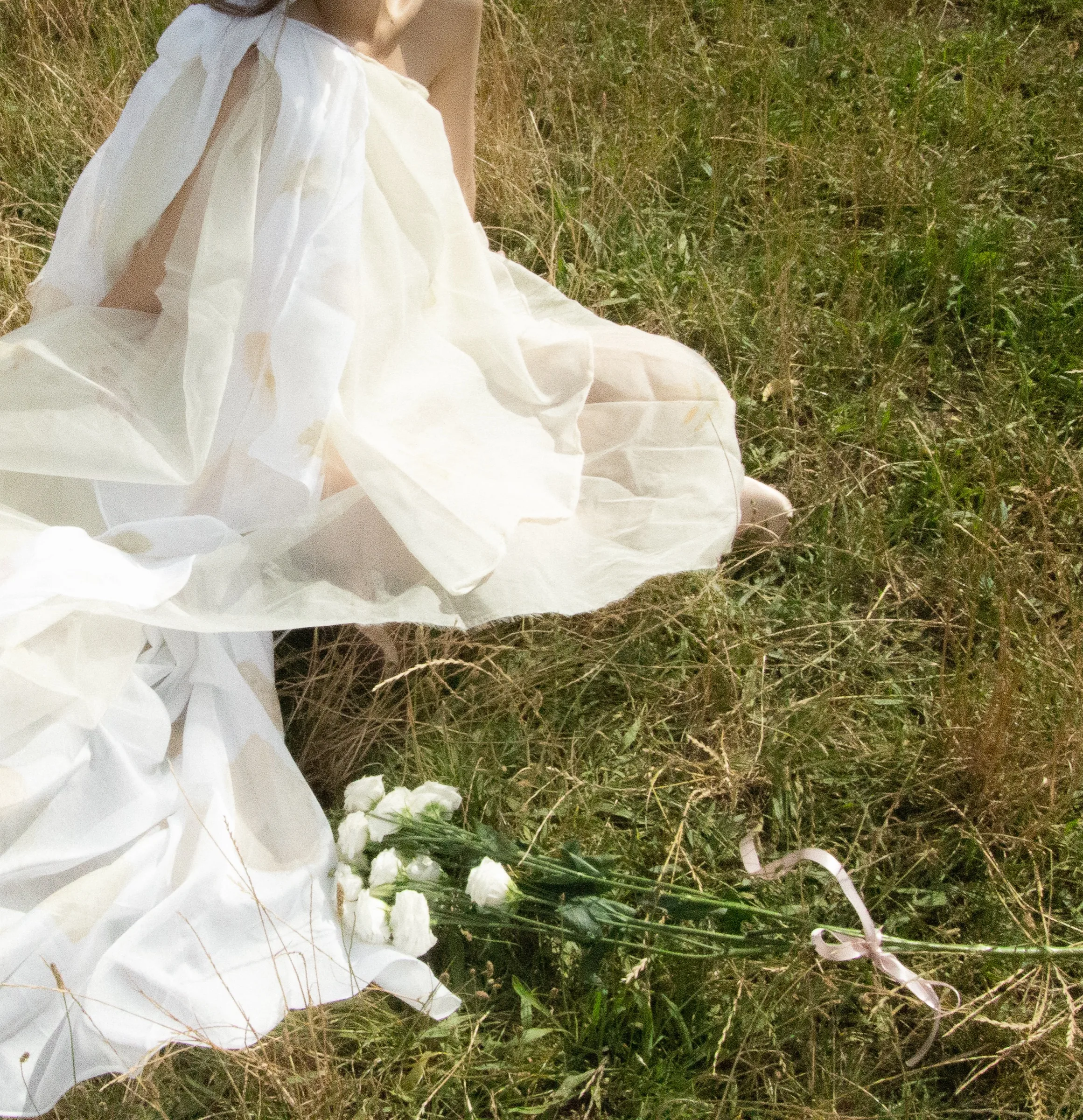 Sheer organza skirt and bare feet folded over a bouquet on the grass