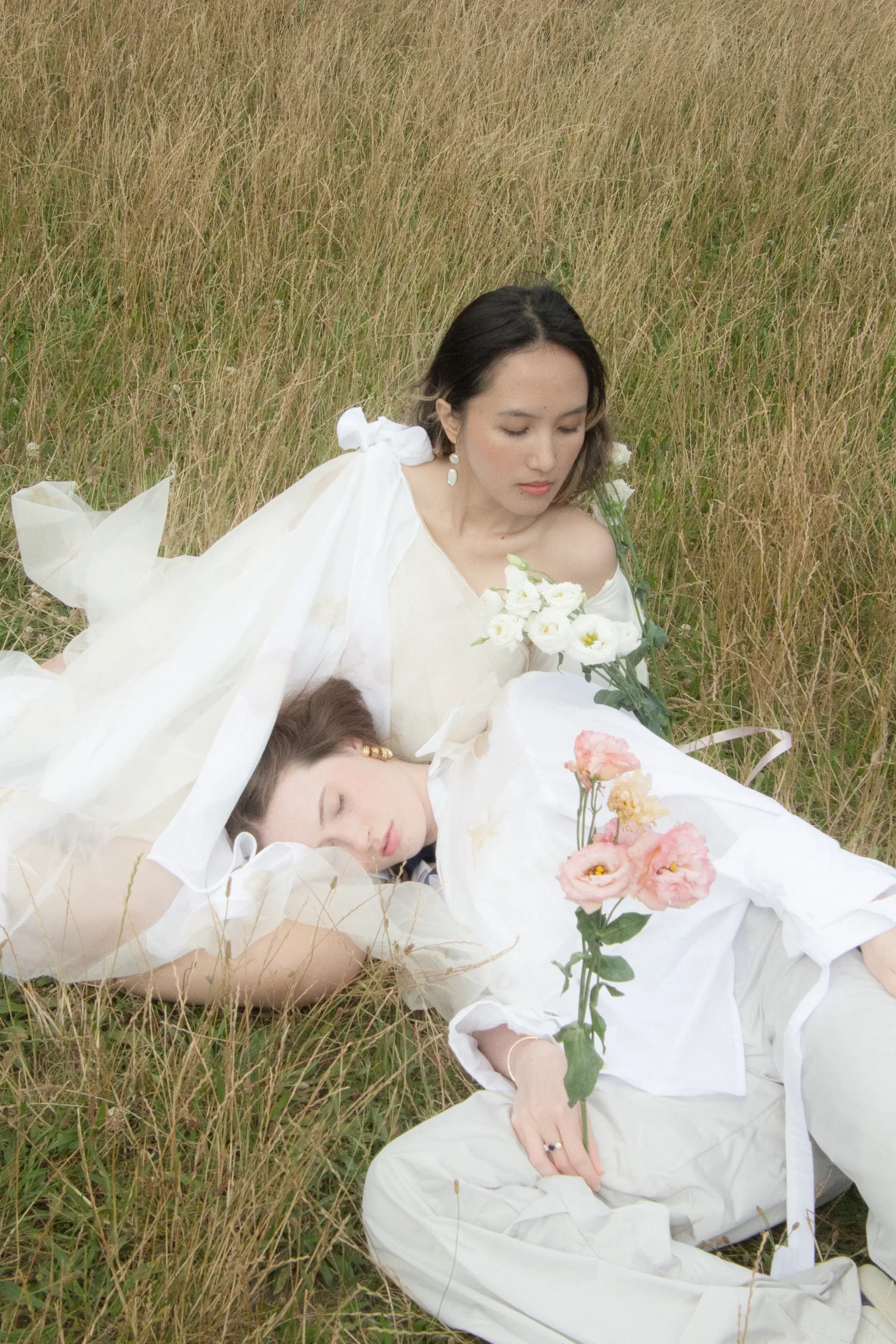 Two figures laid together, a stem of peach ranunculus across white poplin