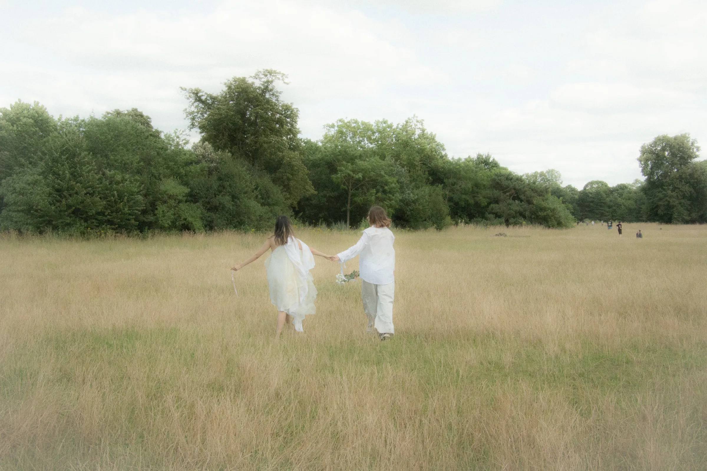 Two models walk away hand in hand through the tall grass