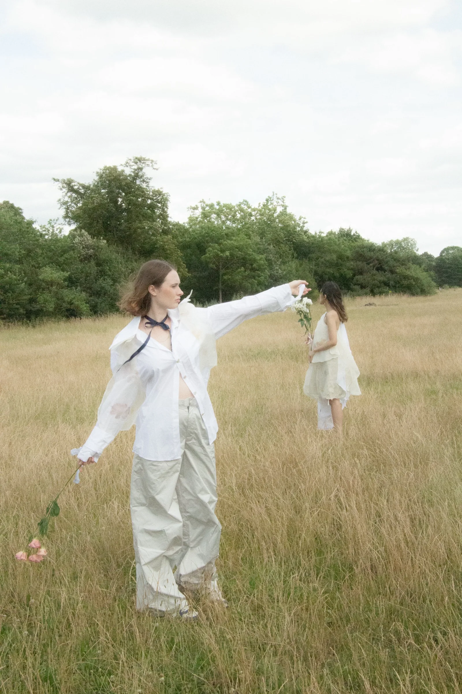 A model extends an arm with a single flower, the other figure beyond