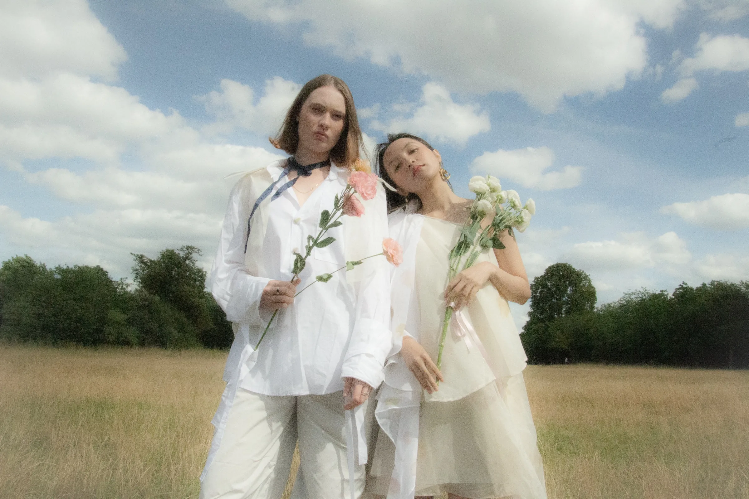 Both models face the camera holding single stems against a clouded sky