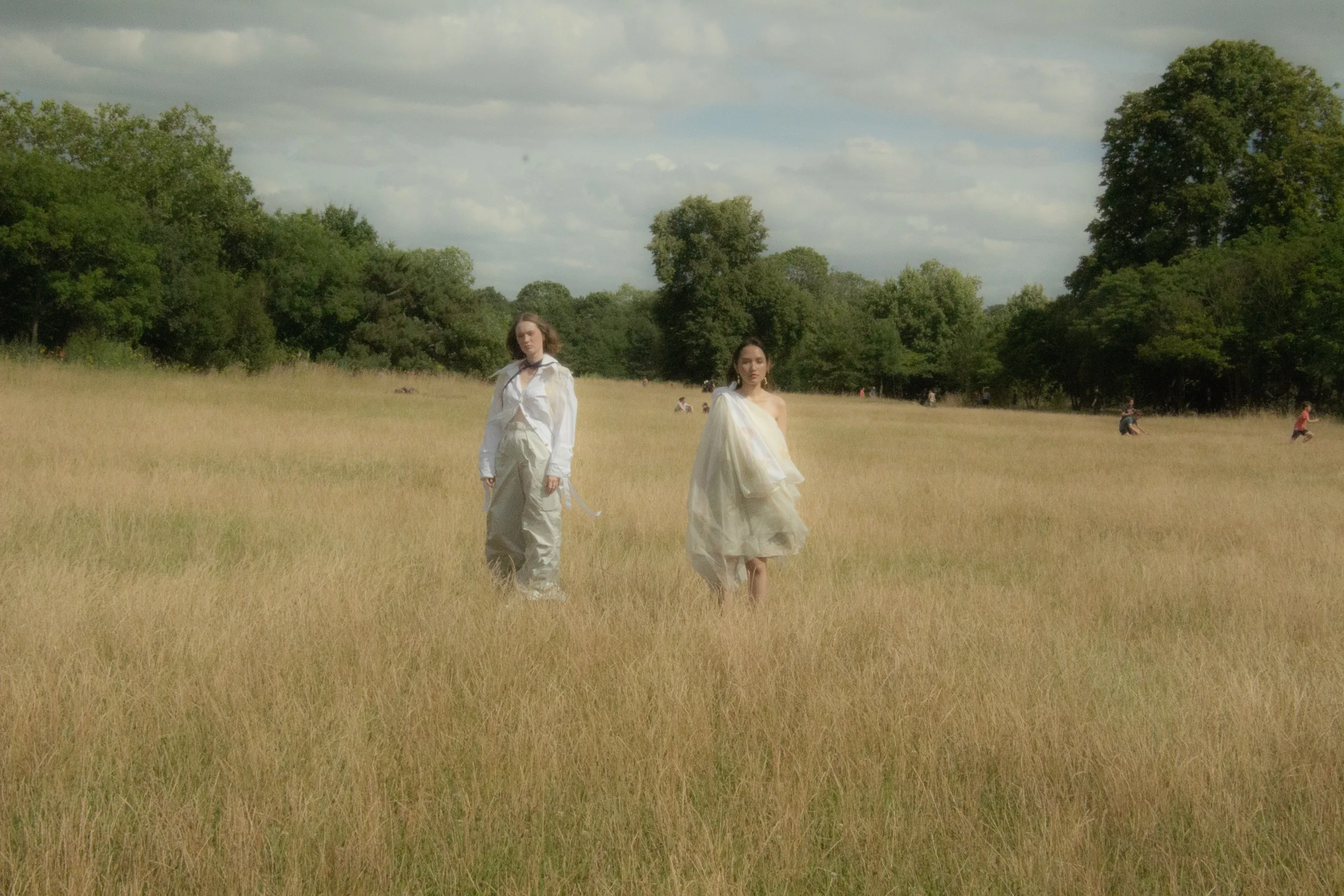 The two models walk toward camera through waist-high grass