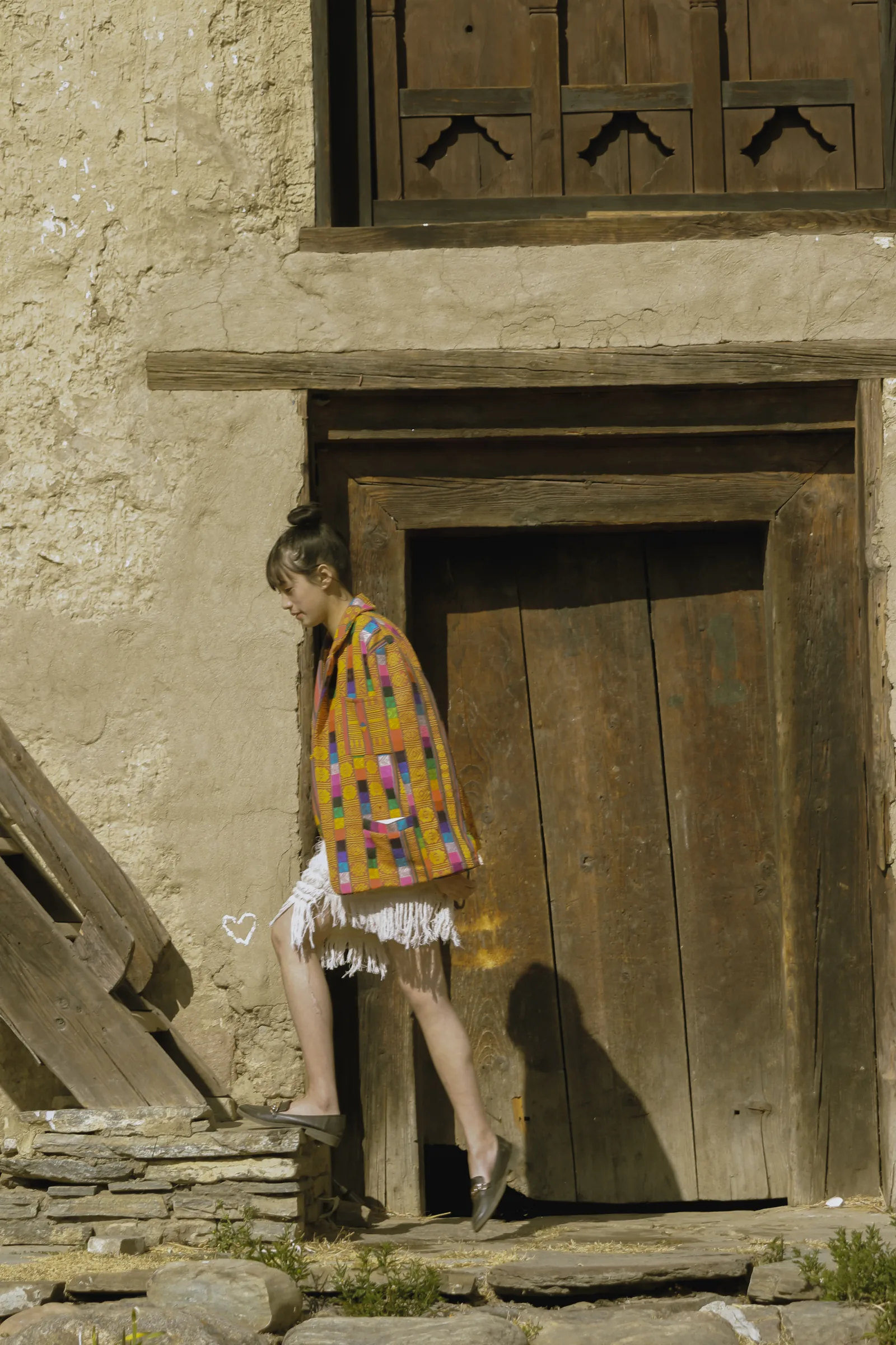 Stepping out of a doorway, the patchwork jacket over a fringed dress