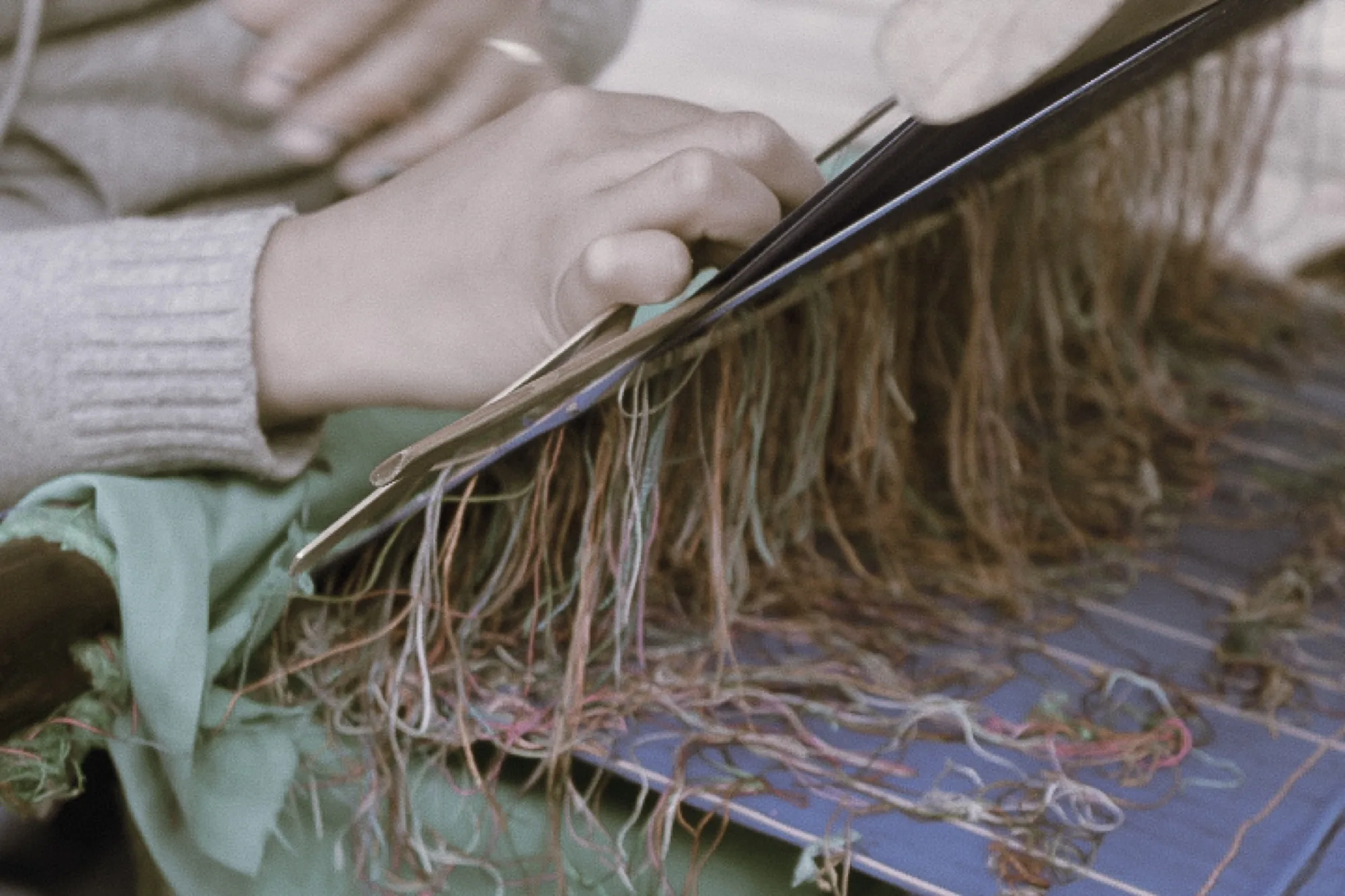 Hands work the sword through the fringe of threads